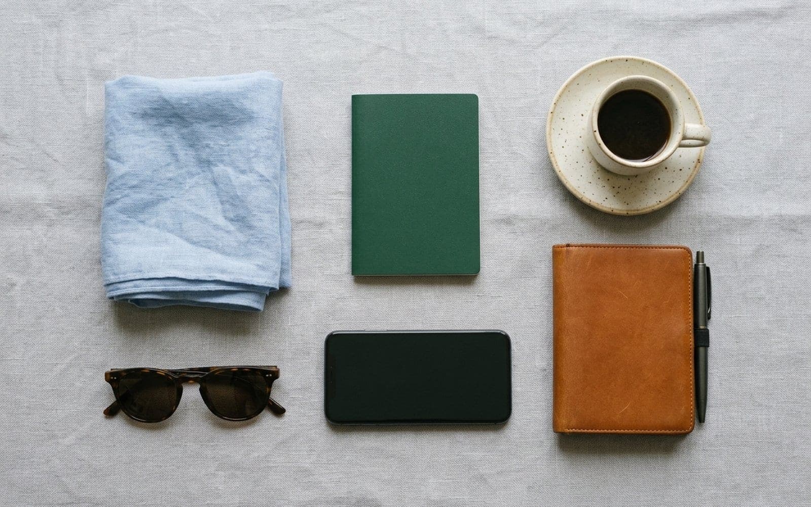 A notebook, phone, wallet, sunglasses and a cup of coffee laid out neatly before a trip.